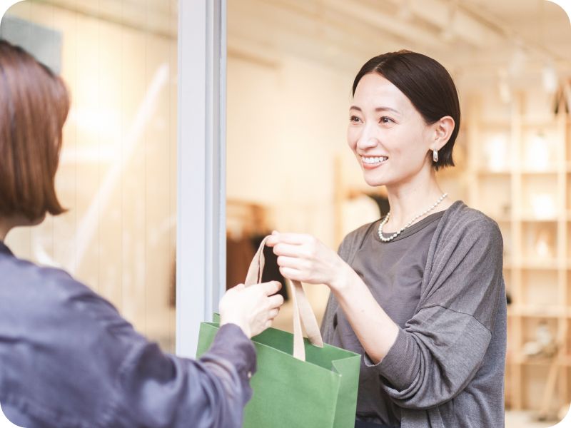 店舗で買い物袋を手渡しする笑顔の女性スタッフ